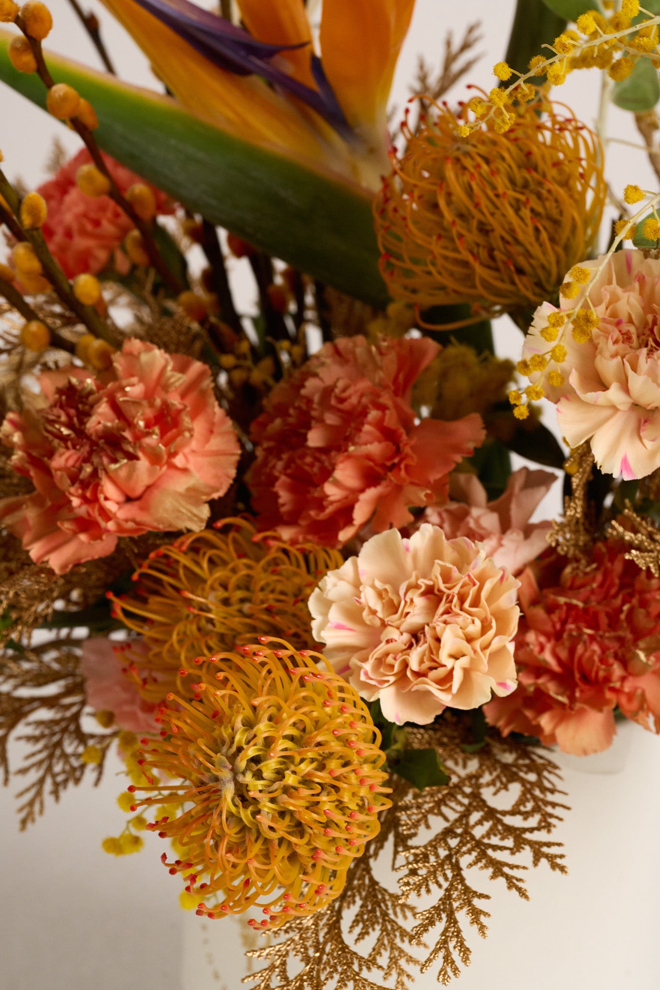 A luxurious floral arrangement featuring bird-of-paradise blooms, golden pussy willows, orange pincushion proteas, and peach-toned carnations. Perfect for Lunar New Year celebrations.