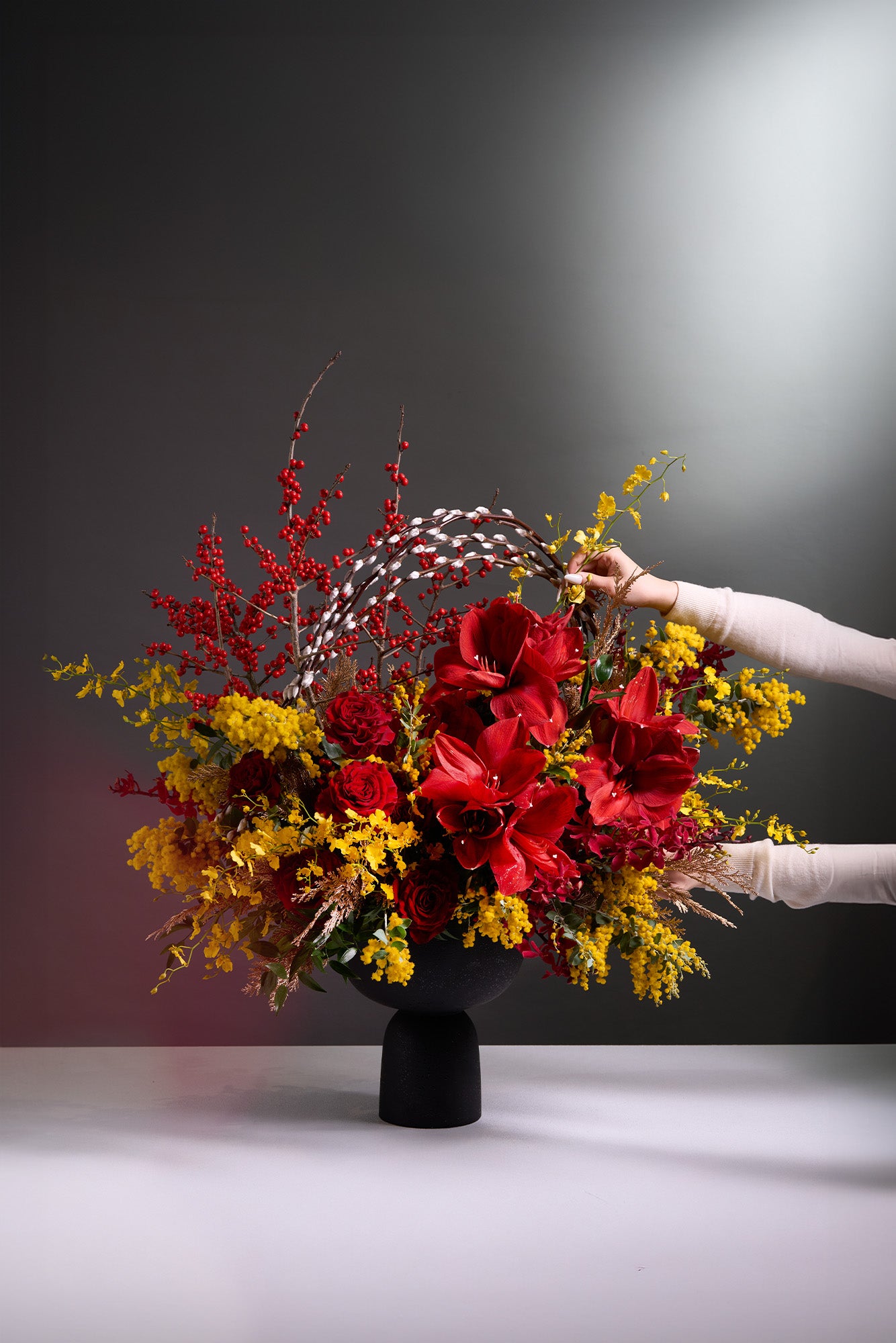 Opulent Blossoms arrangement featuring red amaryllis, deep red roses, yellow oncidium orchids, red berries, and pussy willow, symbolising wealth and prosperity for Lunar New Year.